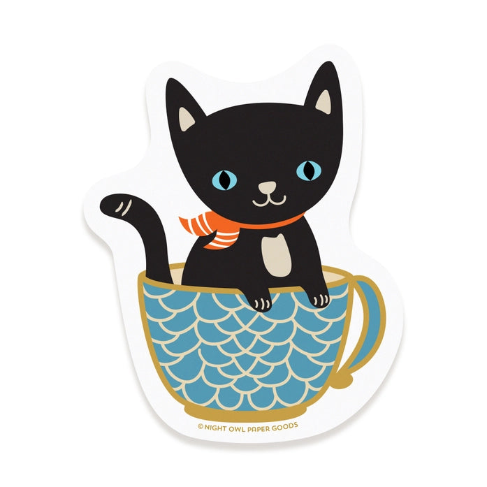 Sticker of a black cat with blue eyes and an orange scarf inside a blue teacup on a white background.