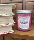 New Book Feeling pink candle in glass jar and lid next to a stack of books in front of a library card catalog