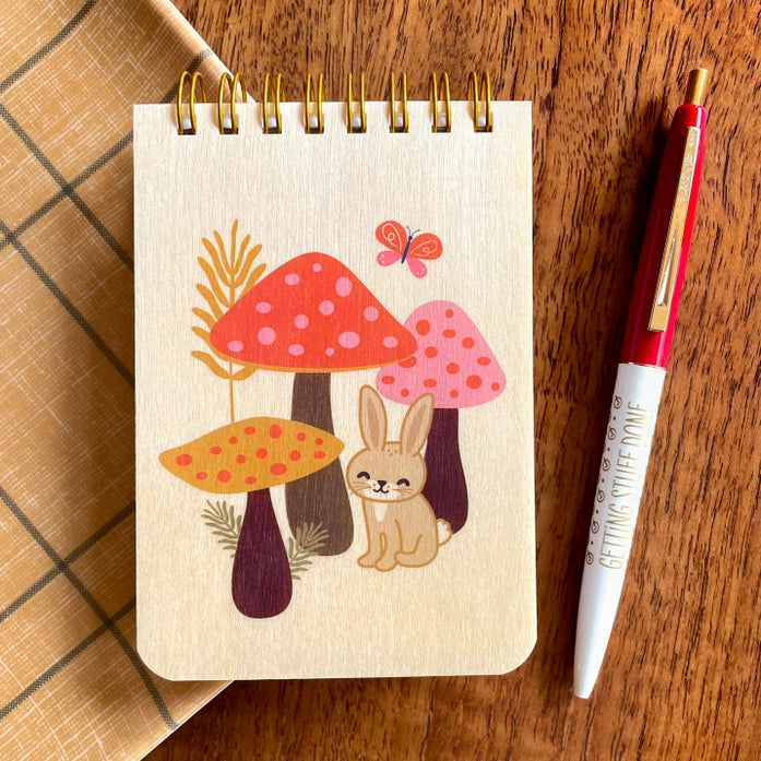 Notebook with mushroom and rabbit illustration on a wooden surface with a pen.