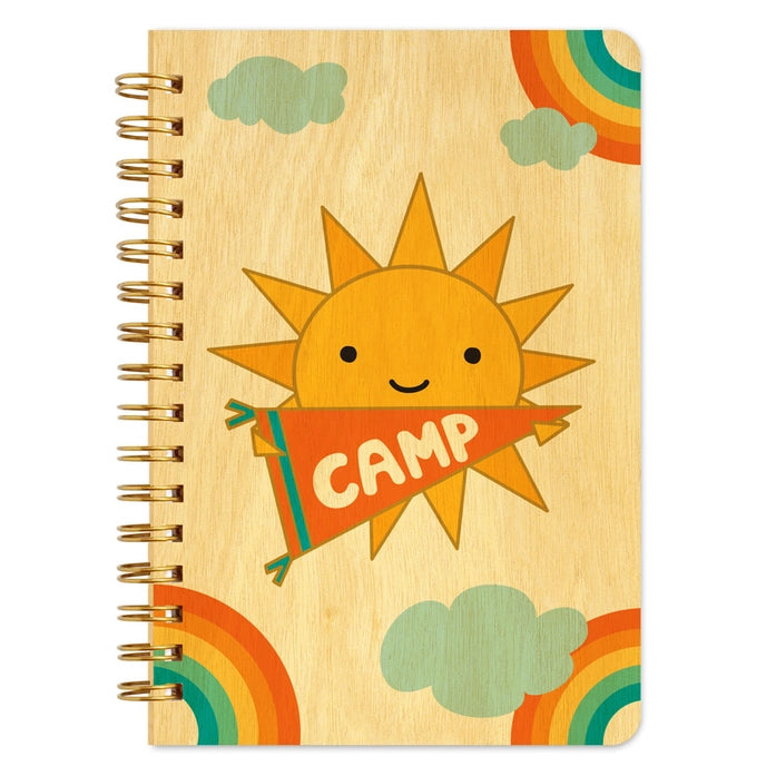 Notebook with a sun design holding a 'Camp' sign on a wooden texture background