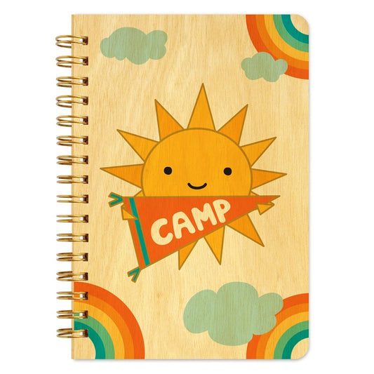 Notebook with a sun design holding a 'Camp' sign on a wooden texture background