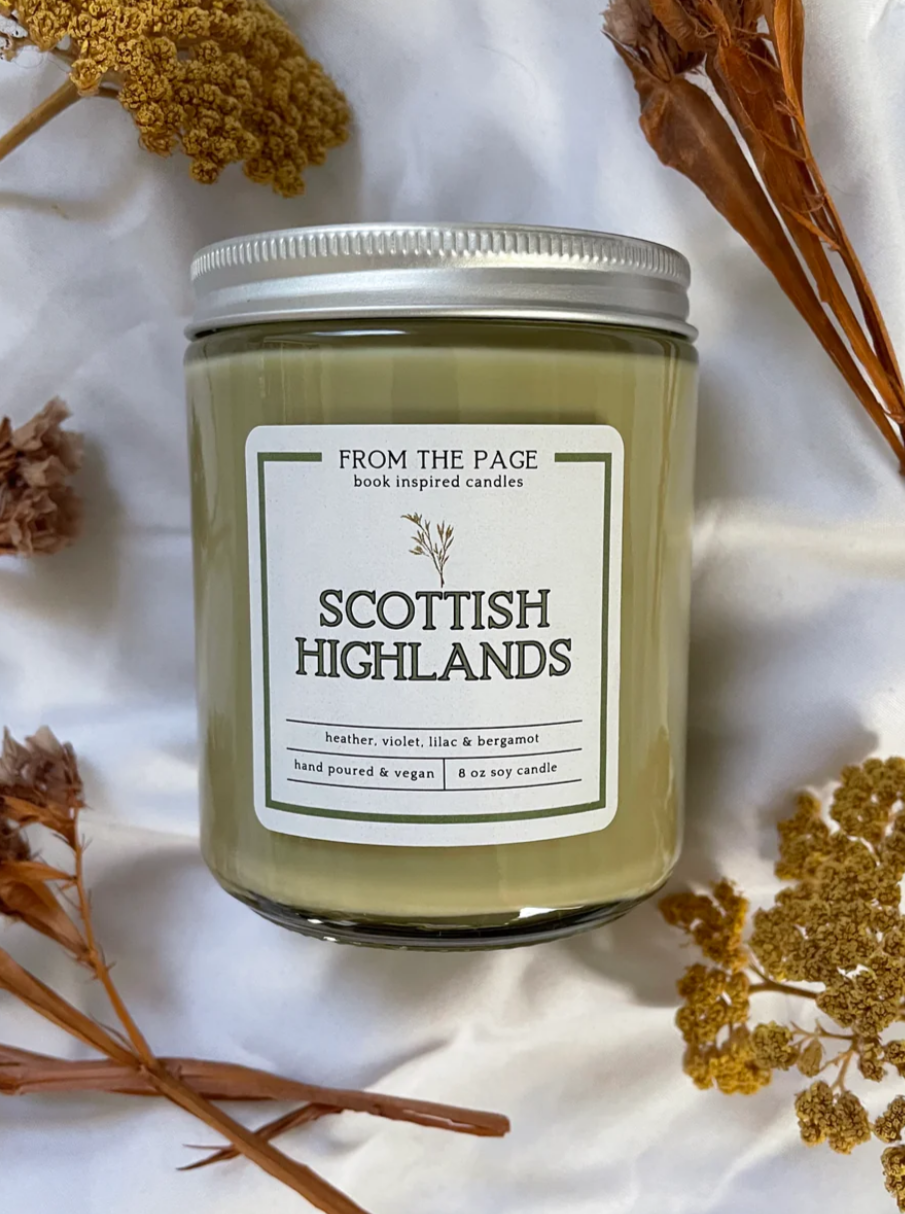 Green Scottish Highlands candle in glass vessel on white cloth background and faux flowers
